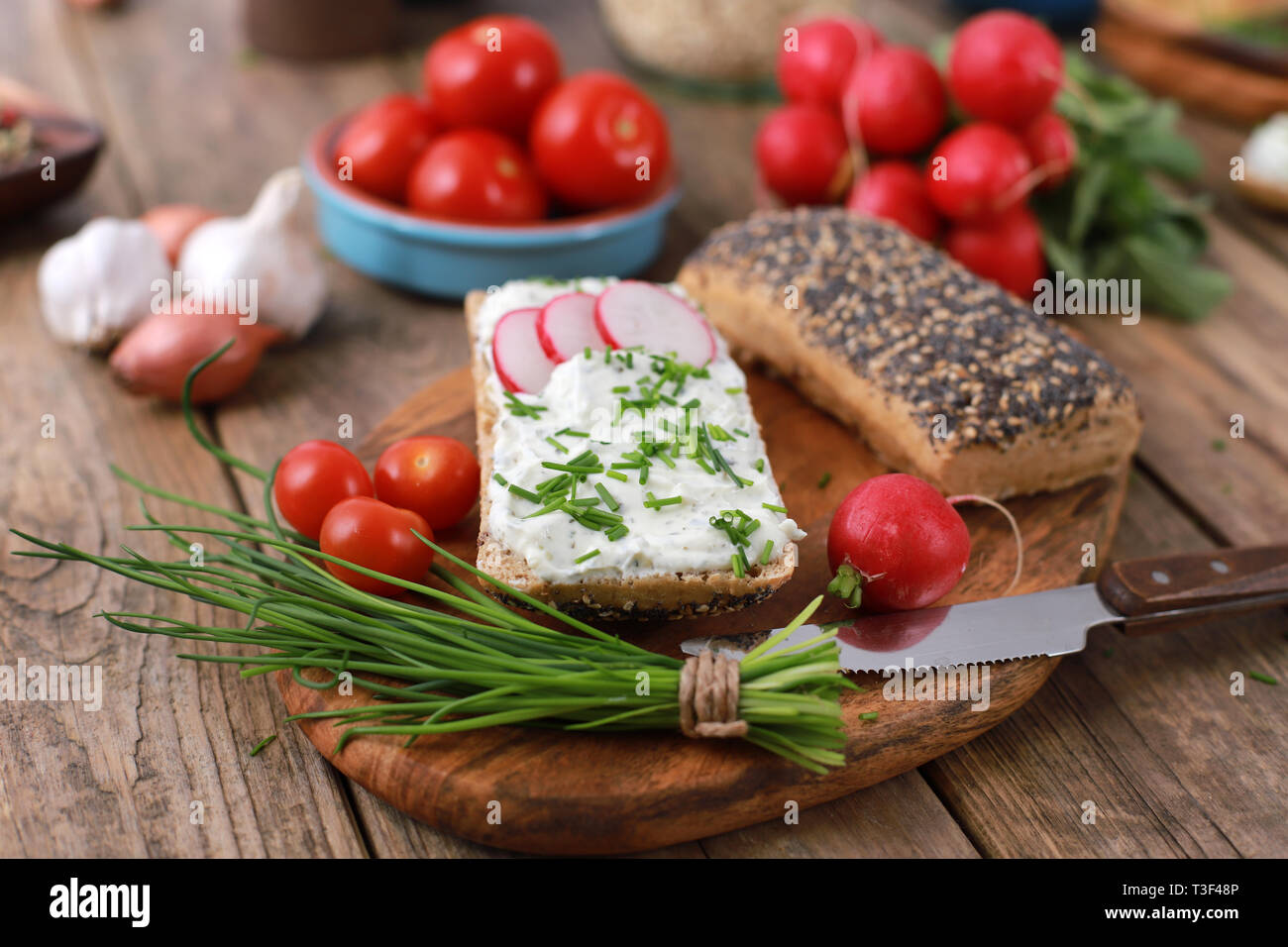 wholemeal roll with quark and fresh chives, radish and tomatoes on a rustic wooden table - healthy breakfast with fresh herbs Stock Photo
