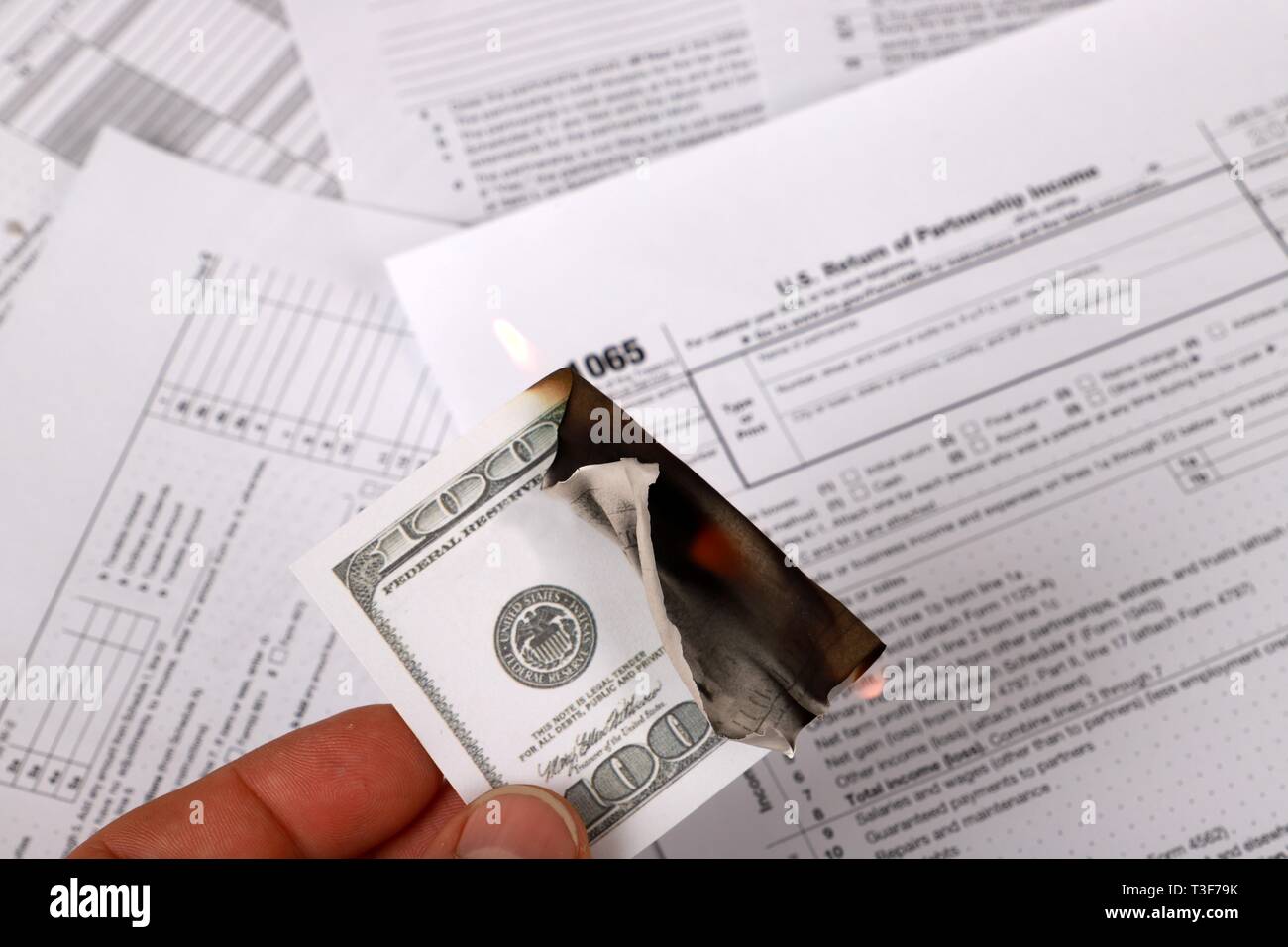 1065 tax form and a burning hundred dollar bill on a Table. US Return for parentship income Stock Photo