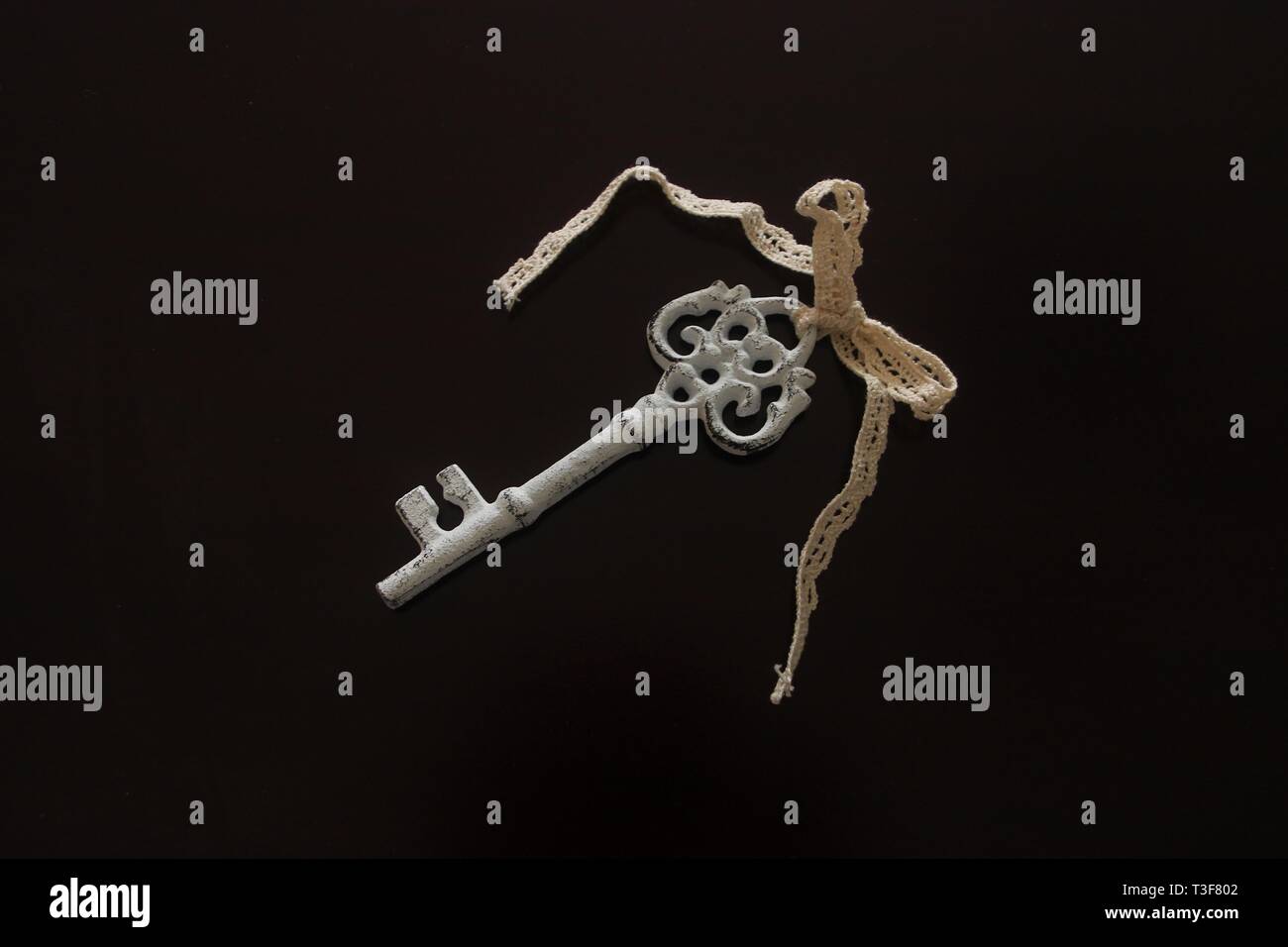 White painted large vintage door key with ribbon and knot isolated on black background Stock