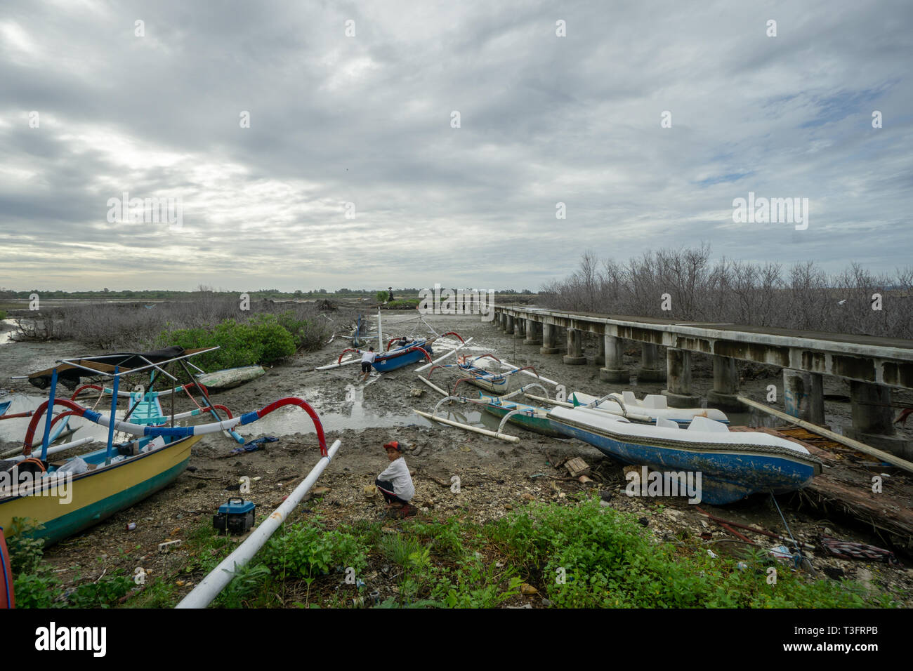 BADUNG,BALI/INDONESIA-MARCH 8 2019:During low tide in Benoa, fishing boats cannot sail. Stuck in a puddle of mud requires the fisherman to push his bo Stock Photo