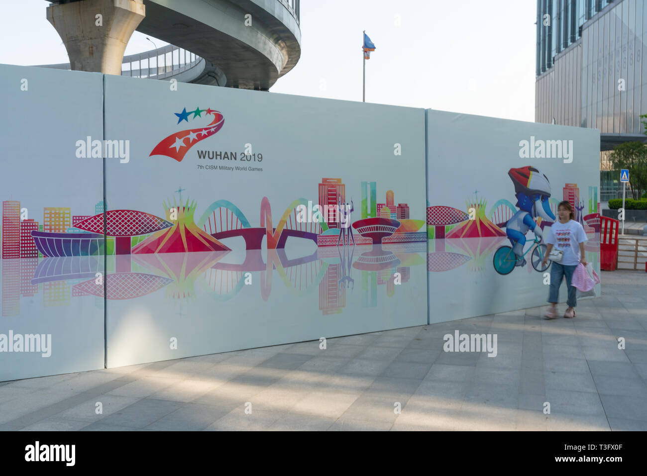 6 April 2019, Wuhan China : Woman walking in front of a giant board advertising the 7th Summer CISM military world games a major sport event in Wuhan  Stock Photo