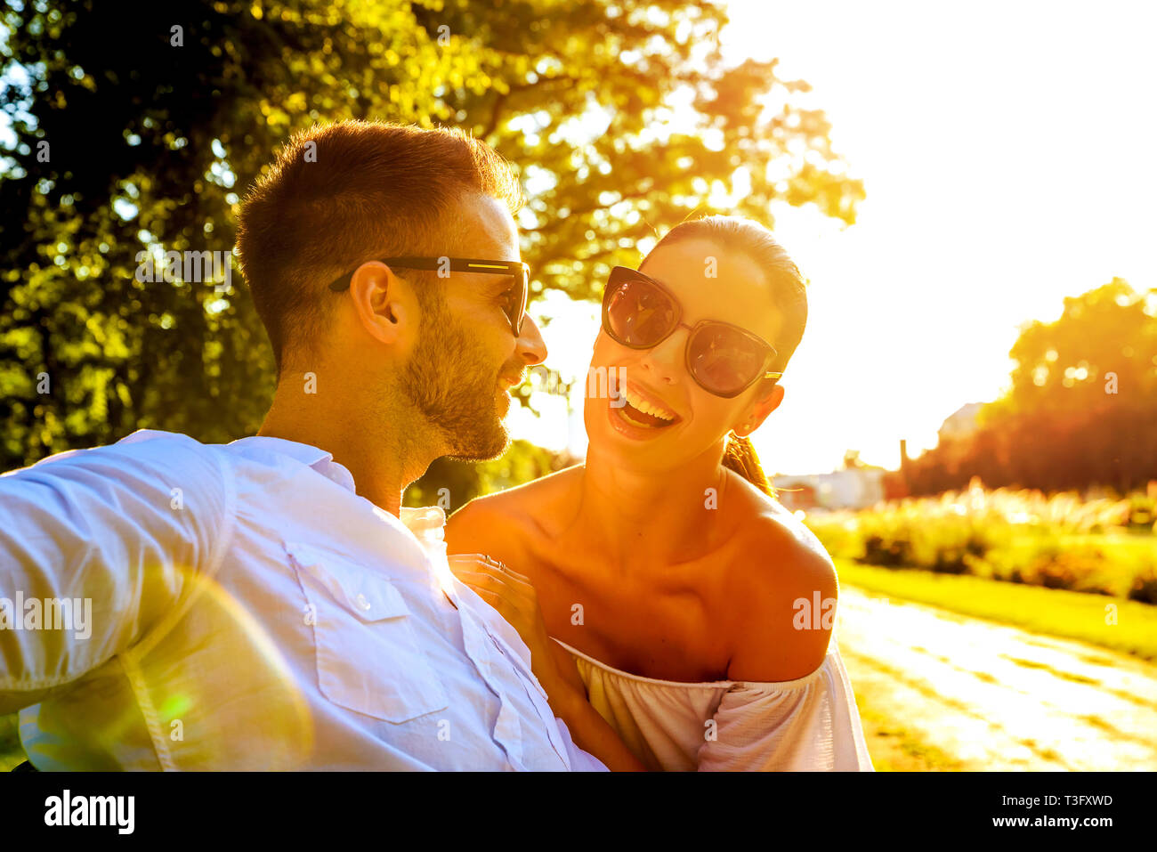 A beautiful young couple sitting on a bench in a park in the sunset ...
