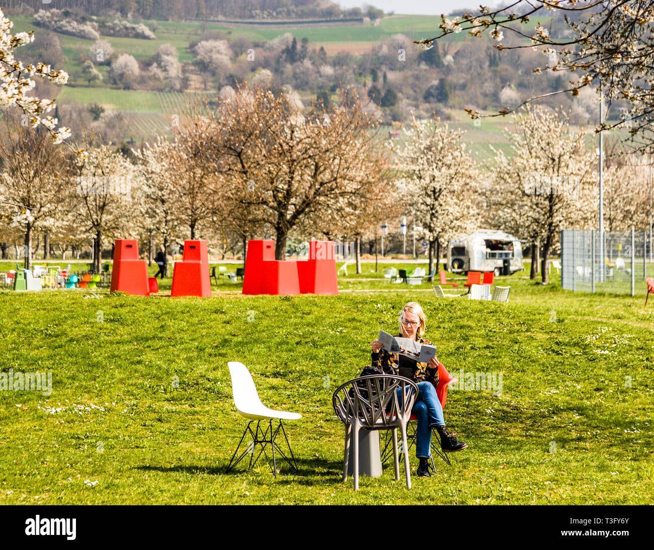 Welcome to the city of chairs. On the lawn in front of the Vitra House, countless designer chairs stand in the landscape. As a visitor, you move your Panton, Eames or a Vegetal by Bouroullec to your liking. In the background, a group of red Stool Tools by Konstantin Grcic. Even further behind the vineyards of Weil. Vitra Campus in Weil am Rhein, Germany Stock Photo