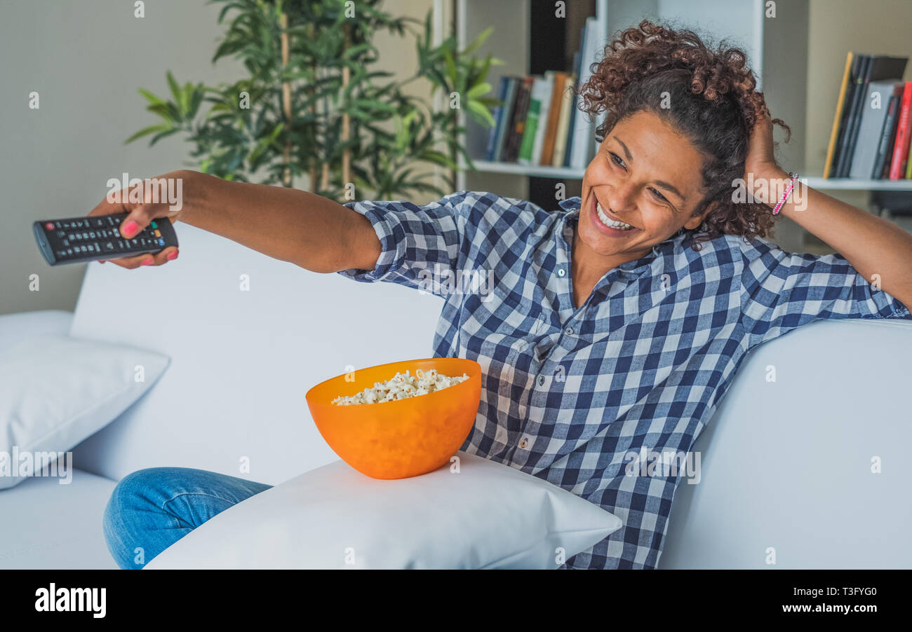 Black woman watching tv at home and holding a remote control Stock Photo