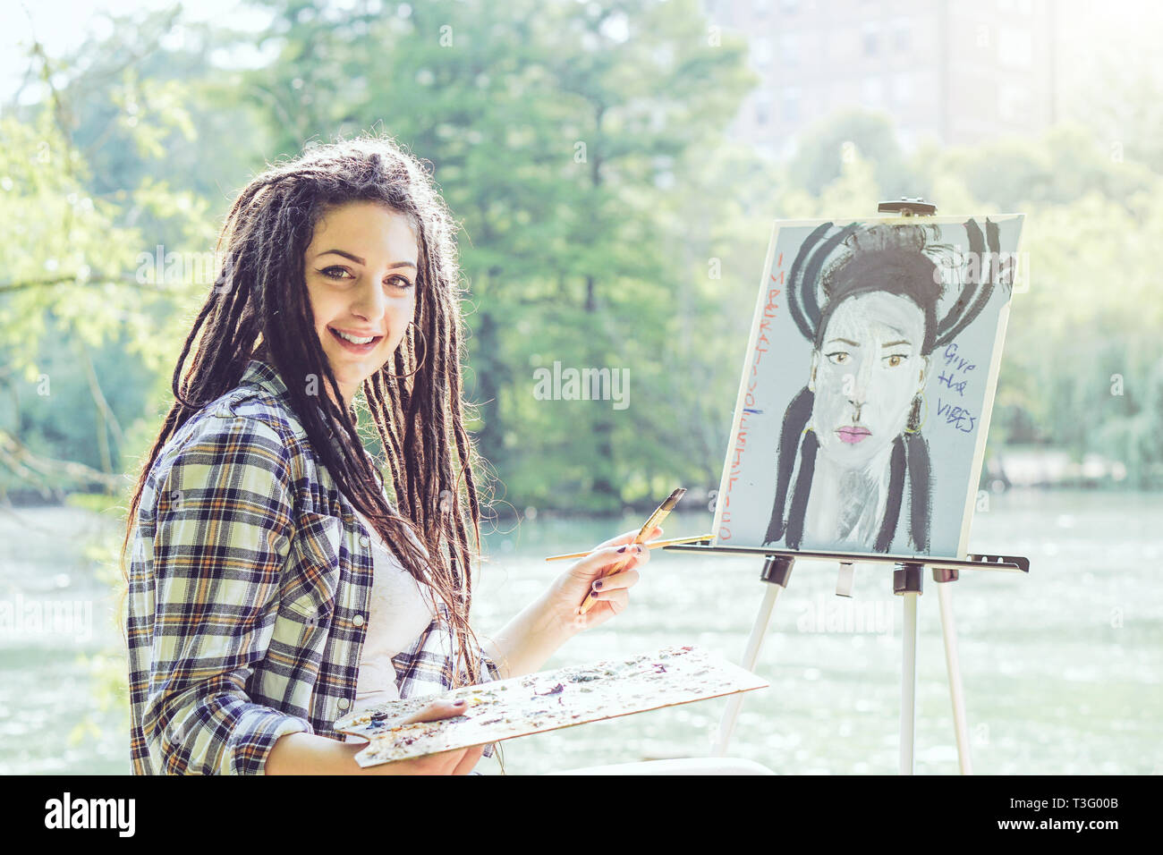 Young artist girl painting a self portrait in a park near lake