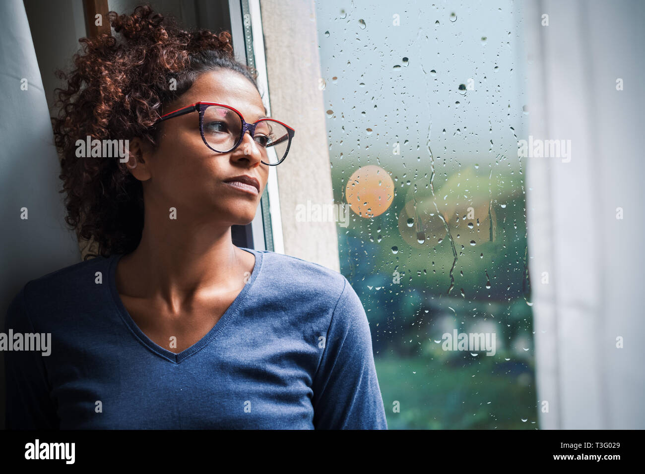 Portrait of pensive black woman standing beside window Stock Photo