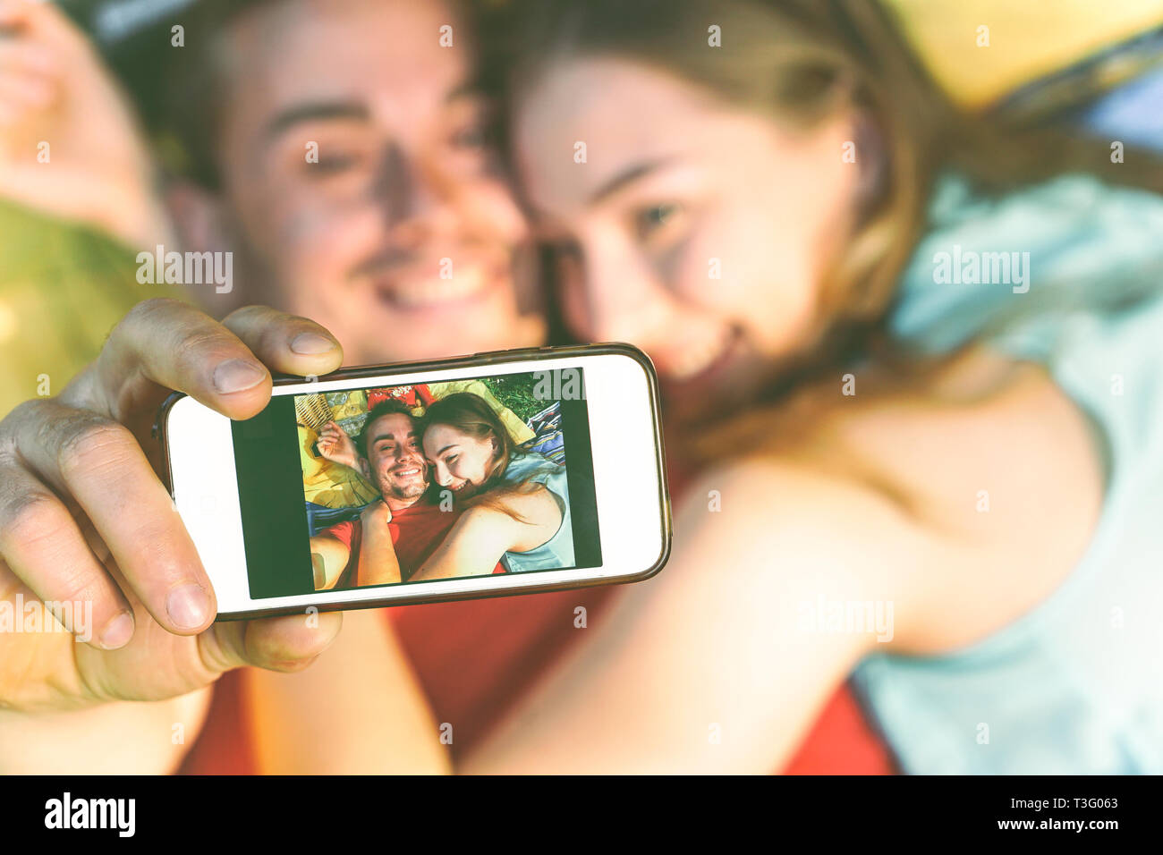 Young couple of lovers taking lying on grass taking a selfie with mobile phone - Happy teenagers in love making a self portrait using smartphone Stock Photo