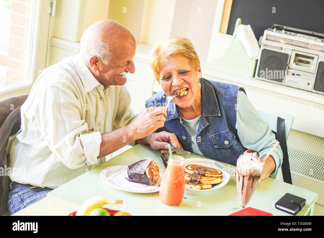 Happy seniors couple eating pancakes in a bar restaurant - Retired people having fun enjoying lunch together - Concept of elderly retired person Stock Photo