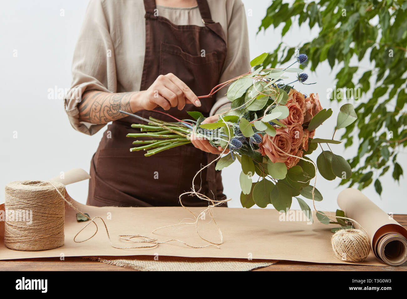 Floral design studio, woman's hands with tatto are making decorative bouquet from fresh natural fragrant flowers roses living coral color on a gray ba Stock Photo