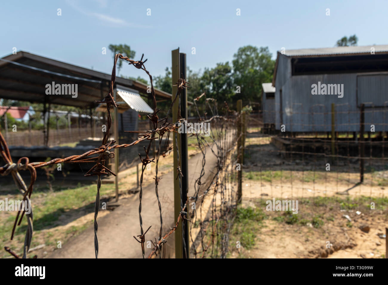 Fence With Barbed Wire In Foreground And Prison Barracks In Background fence-with-barbed-wire-in-foreground-and-prison-barracks-in-background