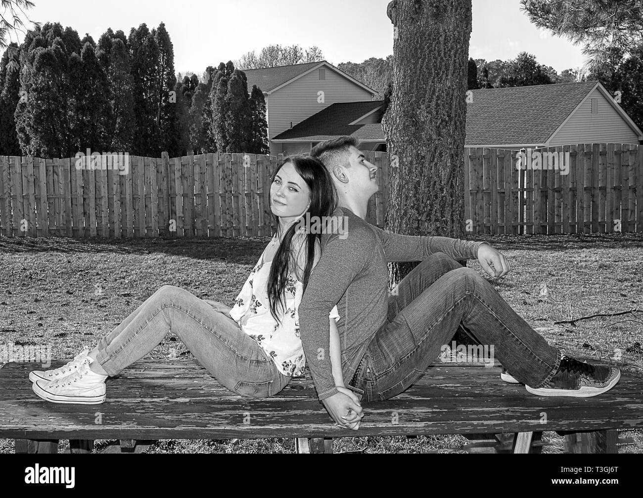 Caucasian couple in love relaxing while sitting on top of picnic able in backyard with their backs to each other.  Black and white image. Stock Photo