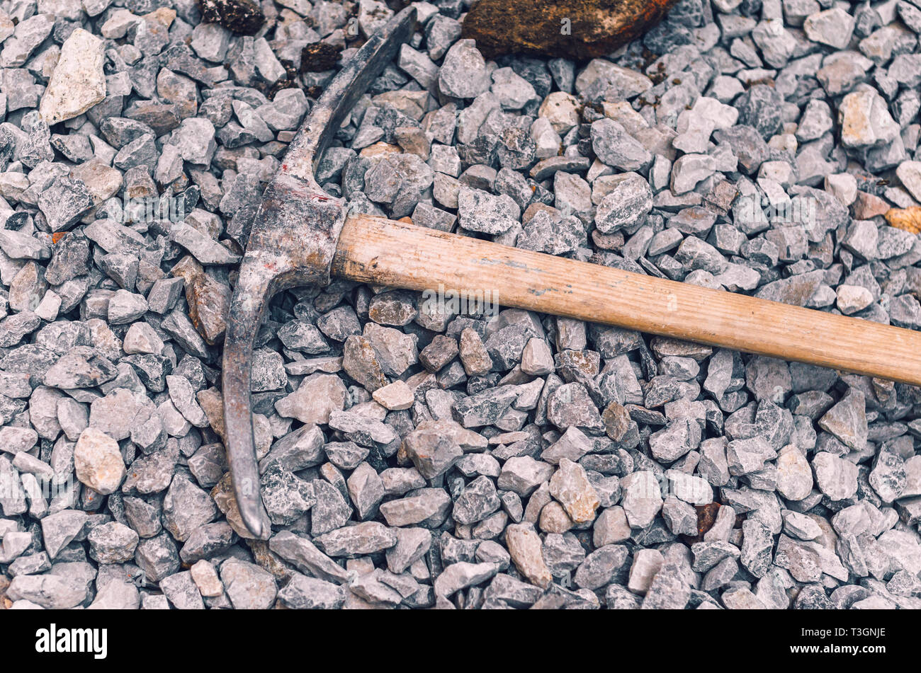 Metal pickaxe on a wooden handle on a pile of small rubble. Dirty