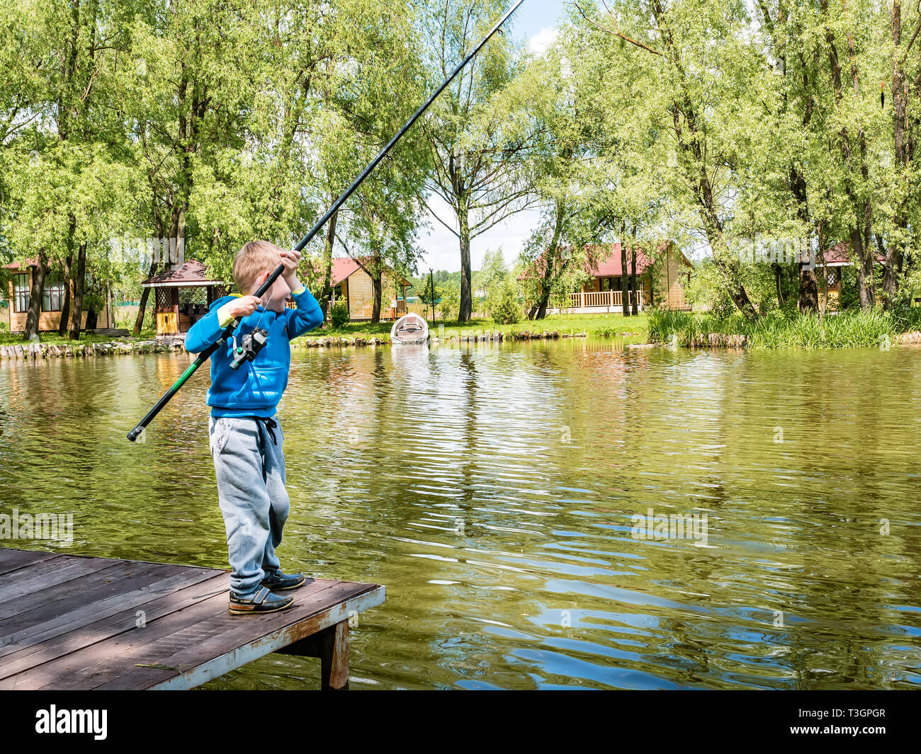 Boy fishing from a wooden dock on a lake or pond pier in a sunny summer  day. Back view of a little 5-year old unrecognizable boy playing with  fishing Stock Photo 