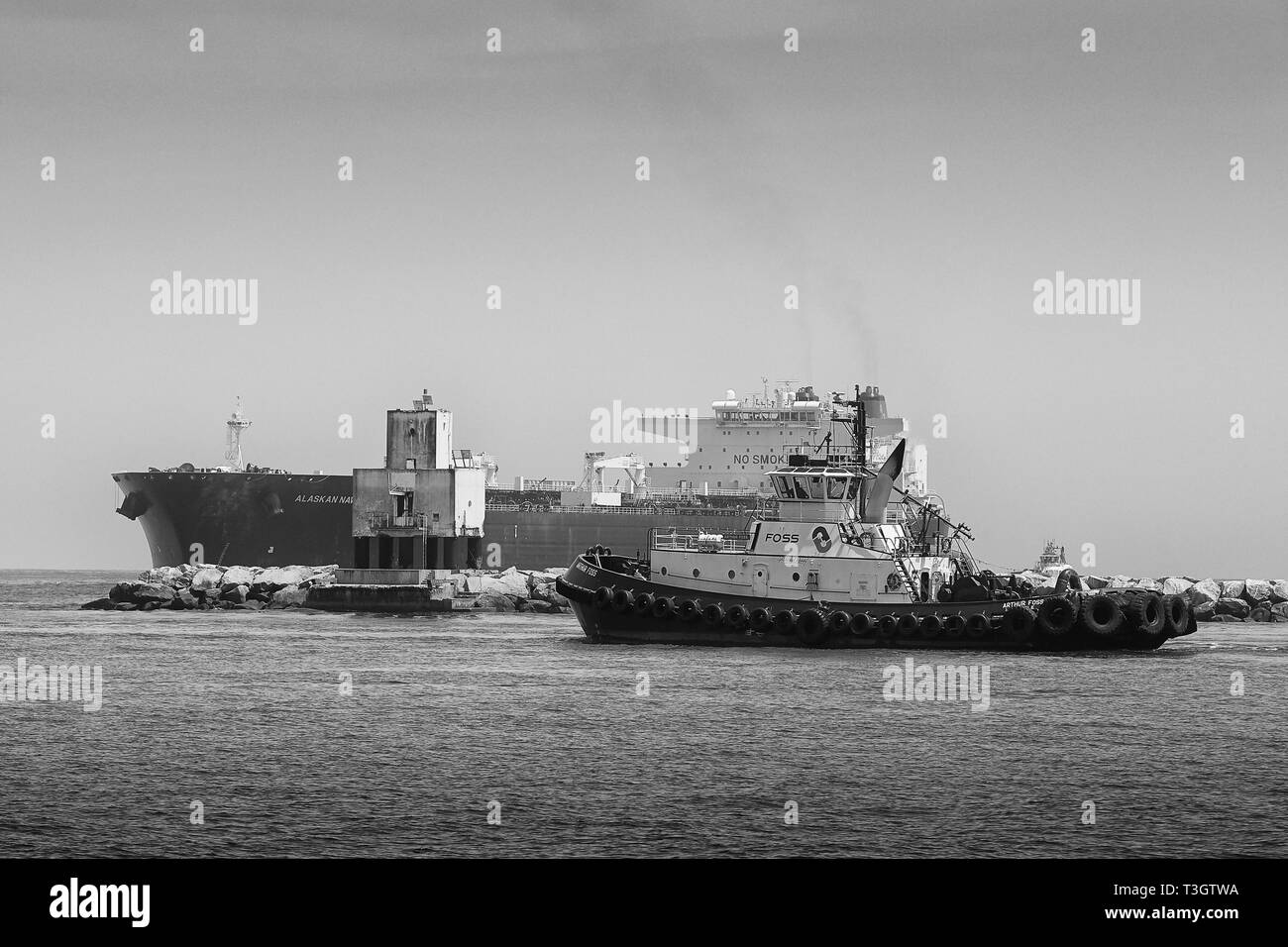 Black And White Photo Of A Tugboat Meeting The Supertanker, ALASKAN NAVIGATOR, At The Long Beach Light, As It Enters The Port Long Beach, California Stock Photo