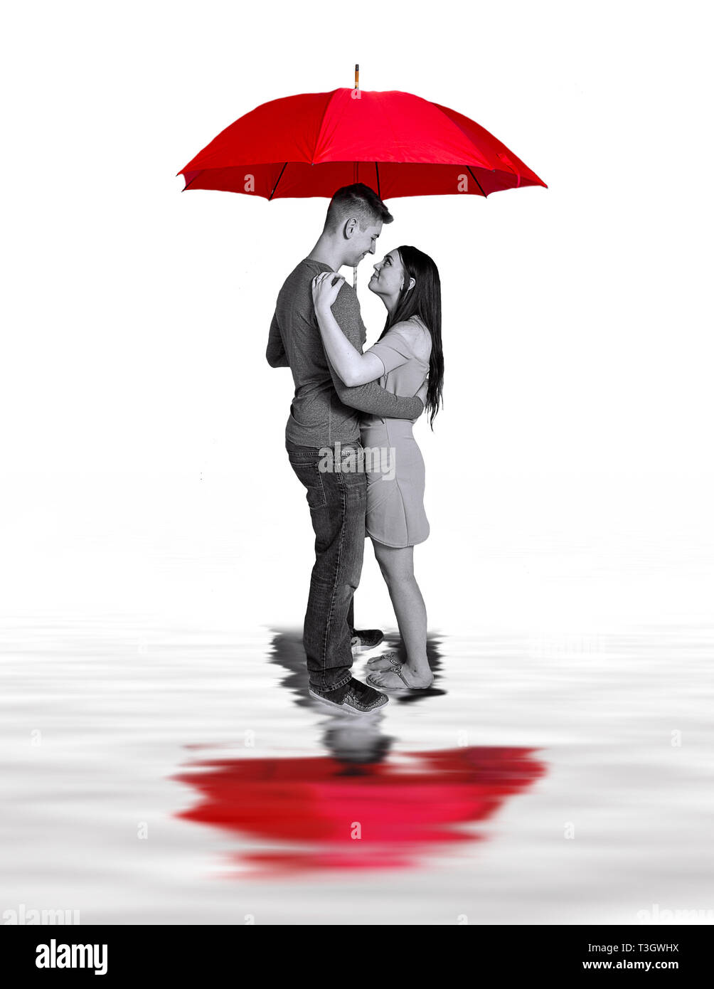 Newly Engaged Couple embracing under large red umbrella with reflections of them in water below.  Concept Image Stock Photo
