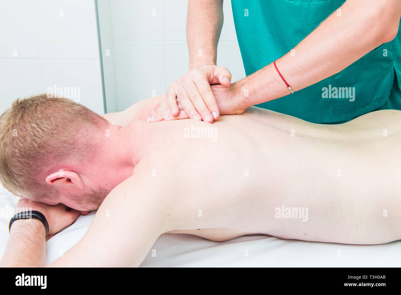 Patient receiving massage from therapist. A chiropractor does deep tissue massage on man's shoulder blade in medical office. Neurological physical exa Stock Photo