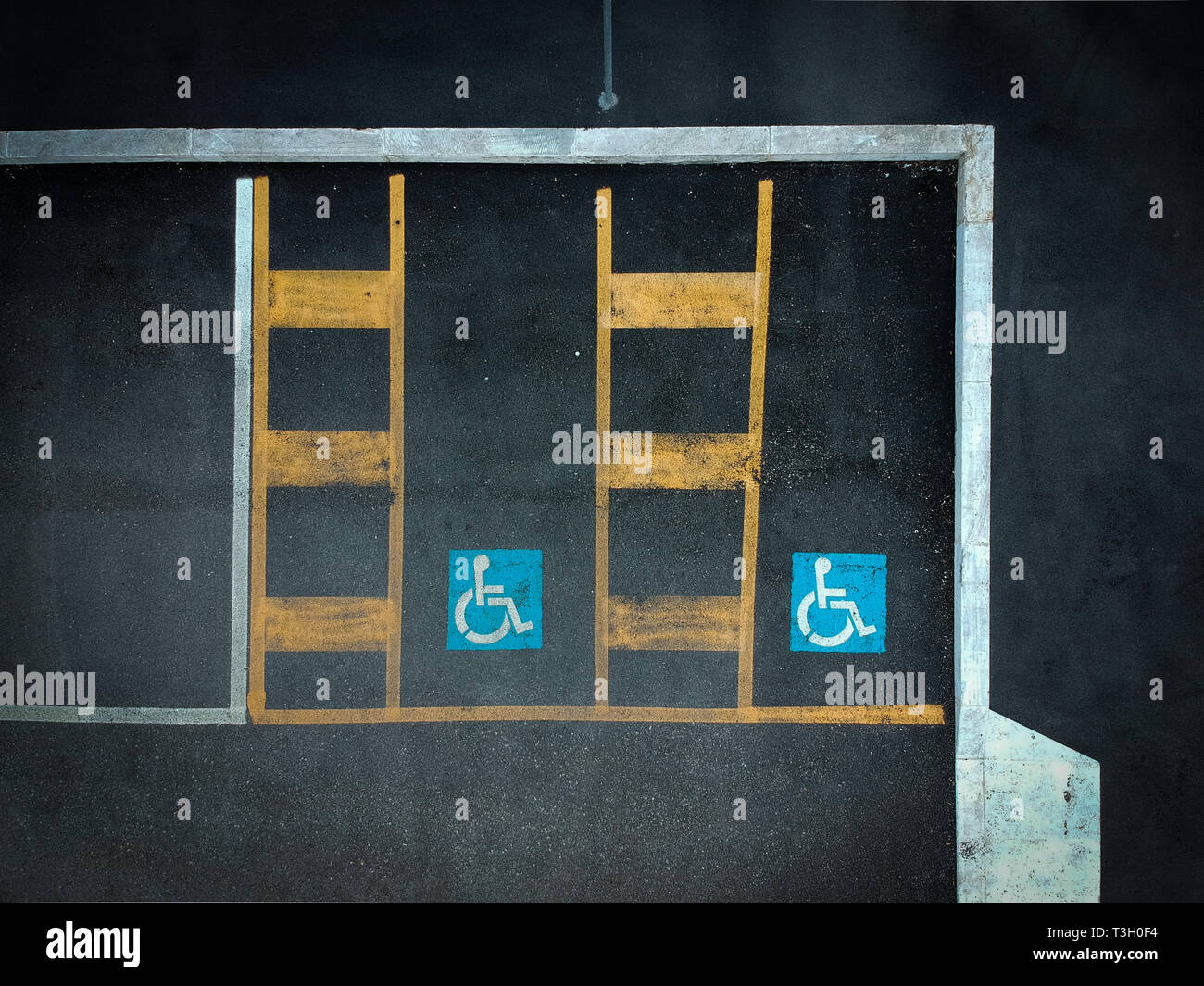 Disabled blue parking sign painted on dark asphalt. Empty handicapped spaces on black. Stock Photo