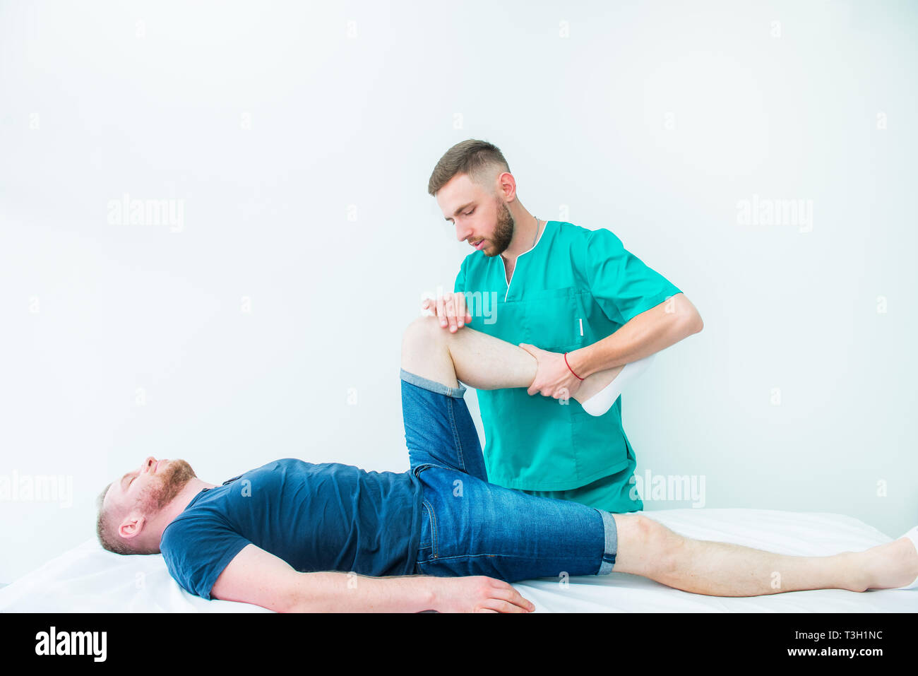 Young male receiving massage from therapist. A chiropractor stretching his patient's legs in medical office. Neurological physical examination. Osteop Stock Photo