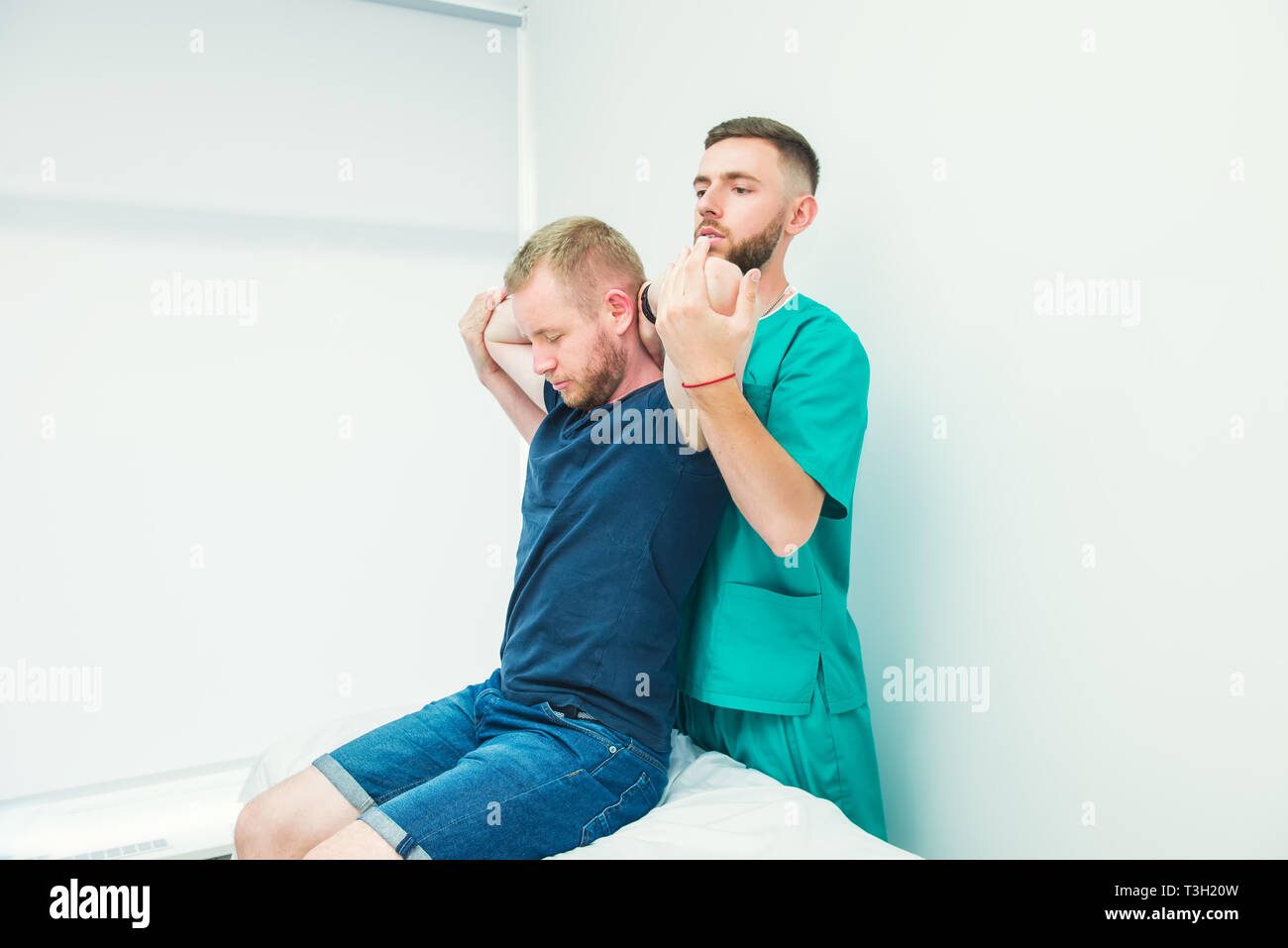 Male patient receiving massage from therapist. A chiropractor stretching his patient's spine and hands in medical office. Neurological physical examin Stock Photo