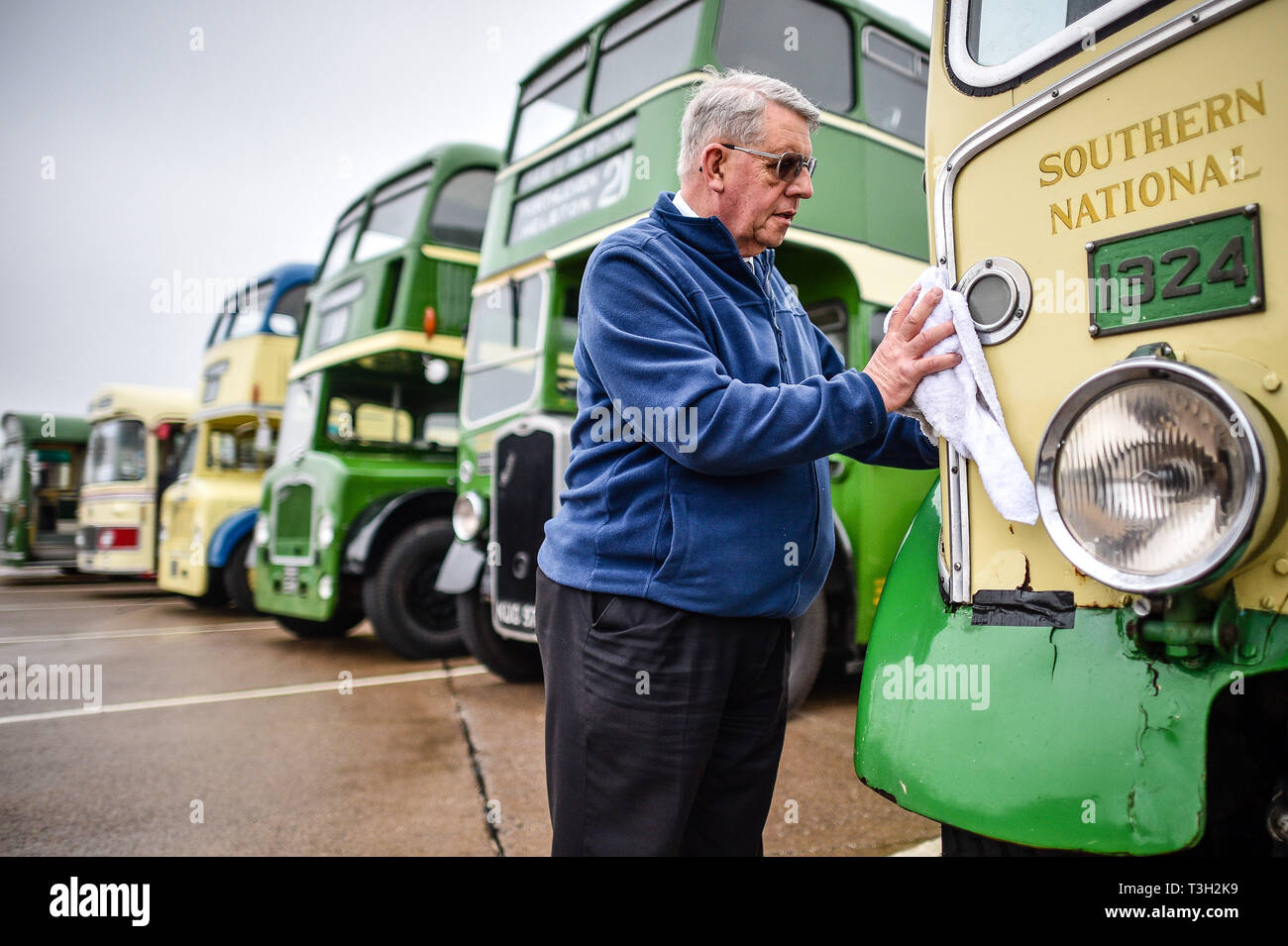 Classic bus driver Nicky Reason cleans the lights on a Bristol L Southern National 1324, as a vintage Bristol vehicle rally prepares to drive from Aerospace Bristol to the Fleet Air Arm Museum in Yeovilton, Somerset, where the Bristol Aeroplane Company produced Bristol Cars. Stock Photo