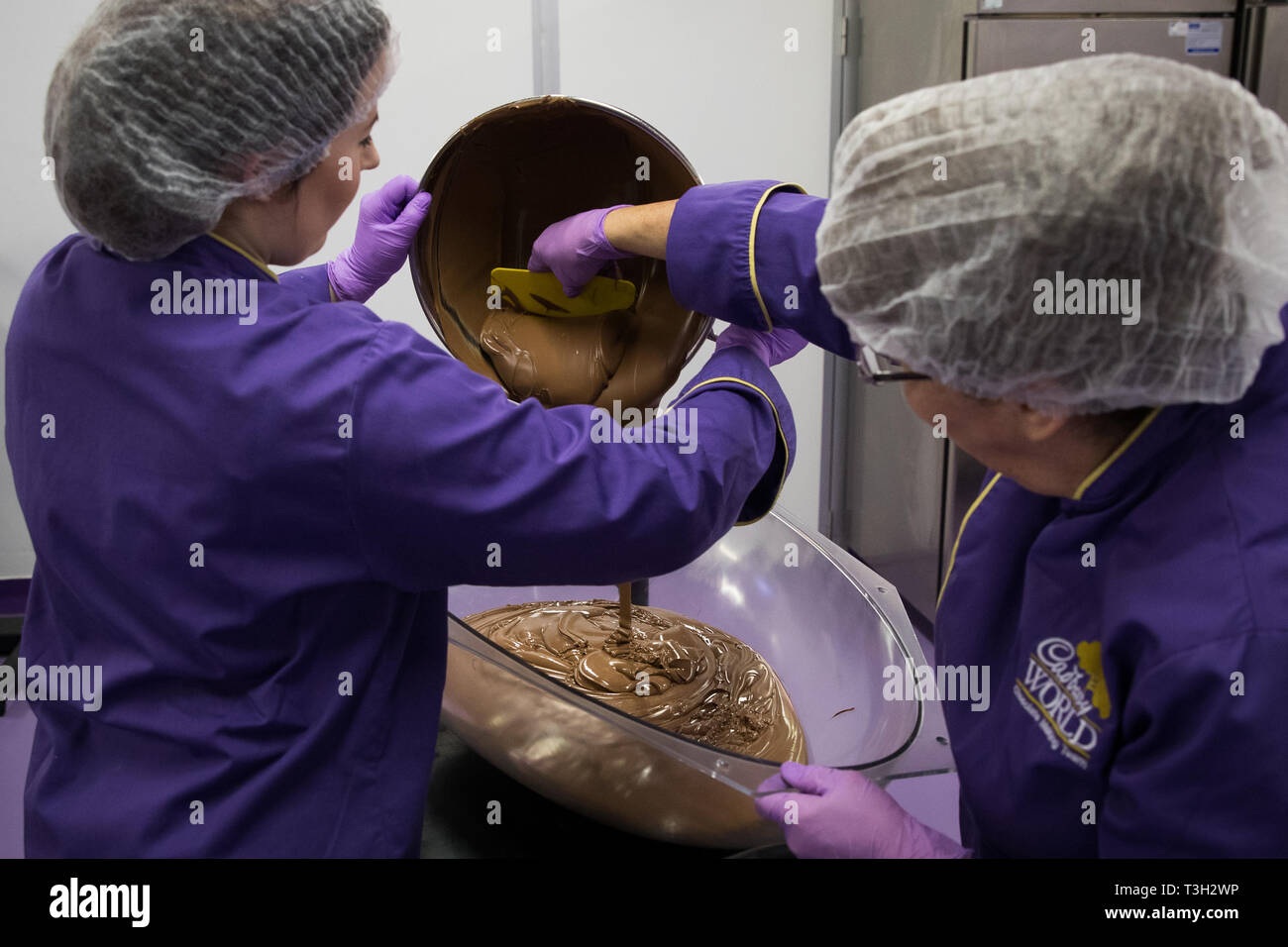 Chocolatiers pour tempered chocolate as they create a giant chocolate egg at Cadbury World in Birmingham to celebrate Easter. Stock Photo