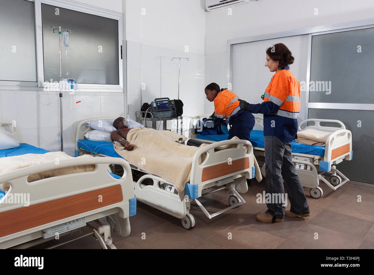 Medical Centre intensive care unit with beds and patient on oxygen showing portable defibrillator and ventilator equipment plus ward doctor and nurse Stock Photo