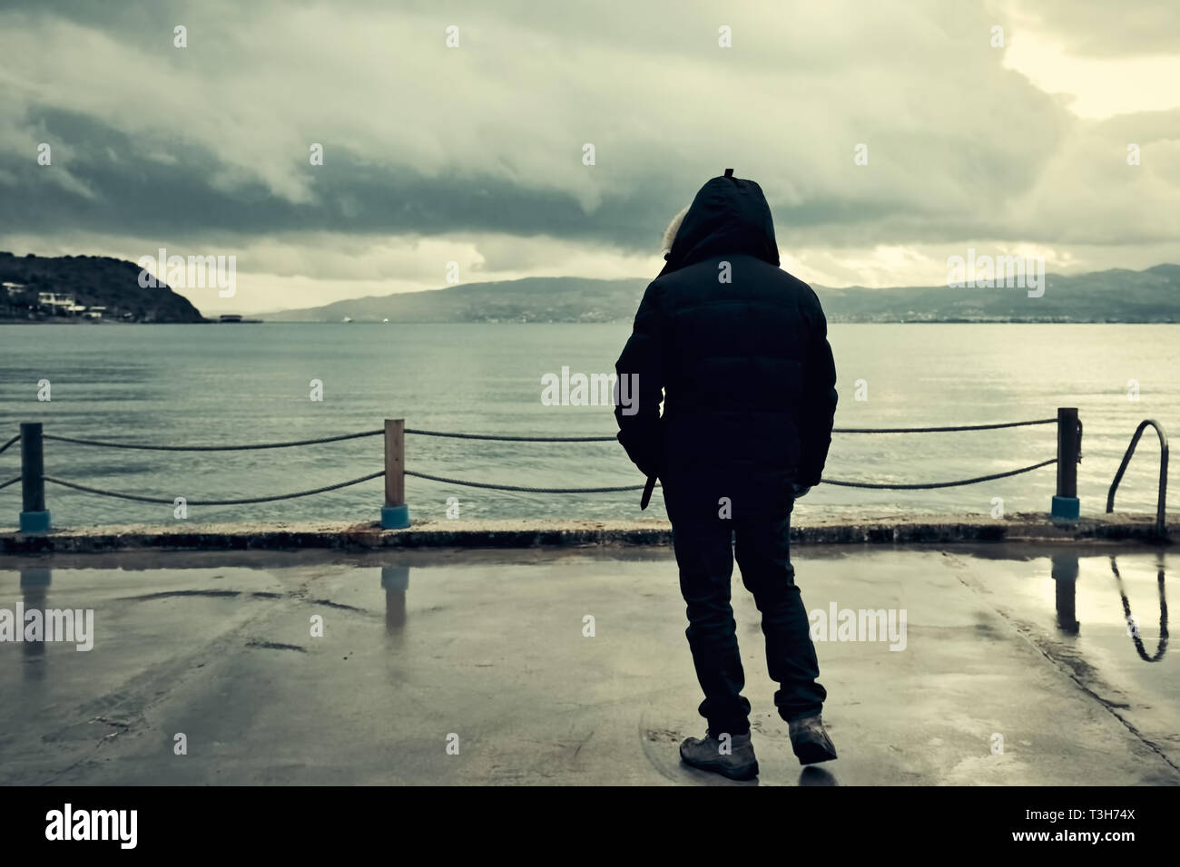 Facing back male person watching the sea on an overcast moody dark and stormy winter day Stock Photo