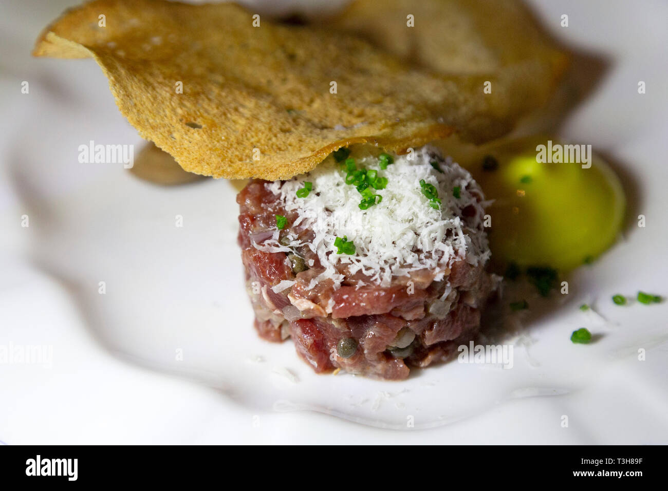 Steak tartare served with a thin slice of crisp bread. The raw meat is topped with grated cheese. Stock Photo