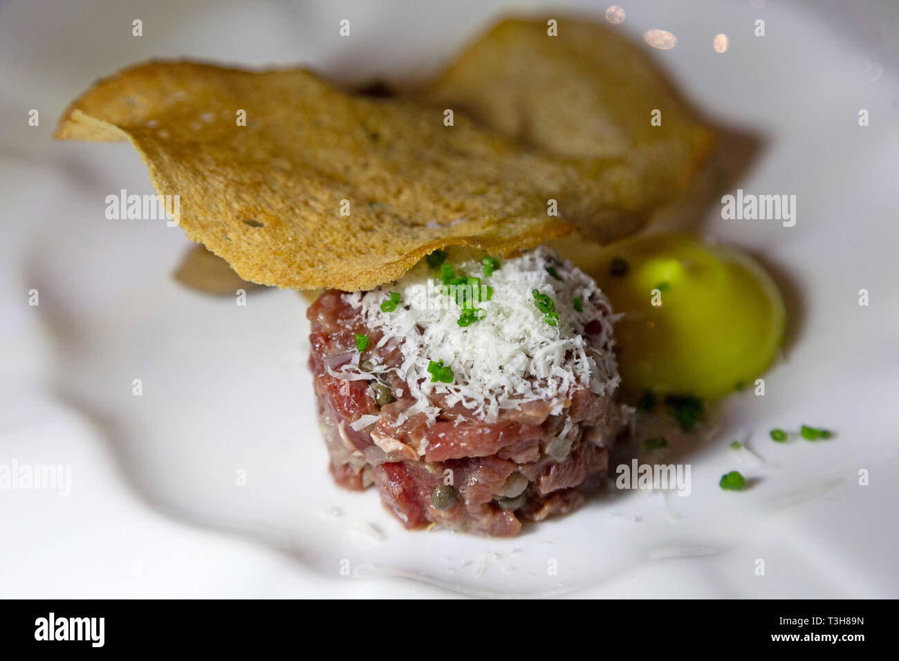 Steak tartare served with a thin slice of crisp bread. The raw meat is topped with grated cheese. Stock Photo
