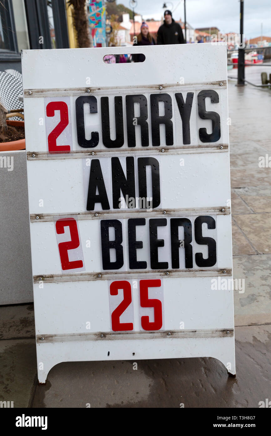 Sign in Whitby, North Yorkshire. The sign advertises a beer and curry package that incorrectly uses 'currys' for the plural of curry. Stock Photo