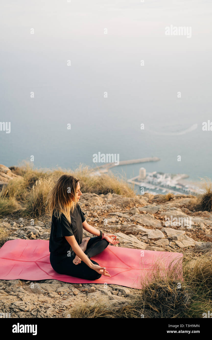 Beautiful young woman doing yoga at the top of the mountain with views ...