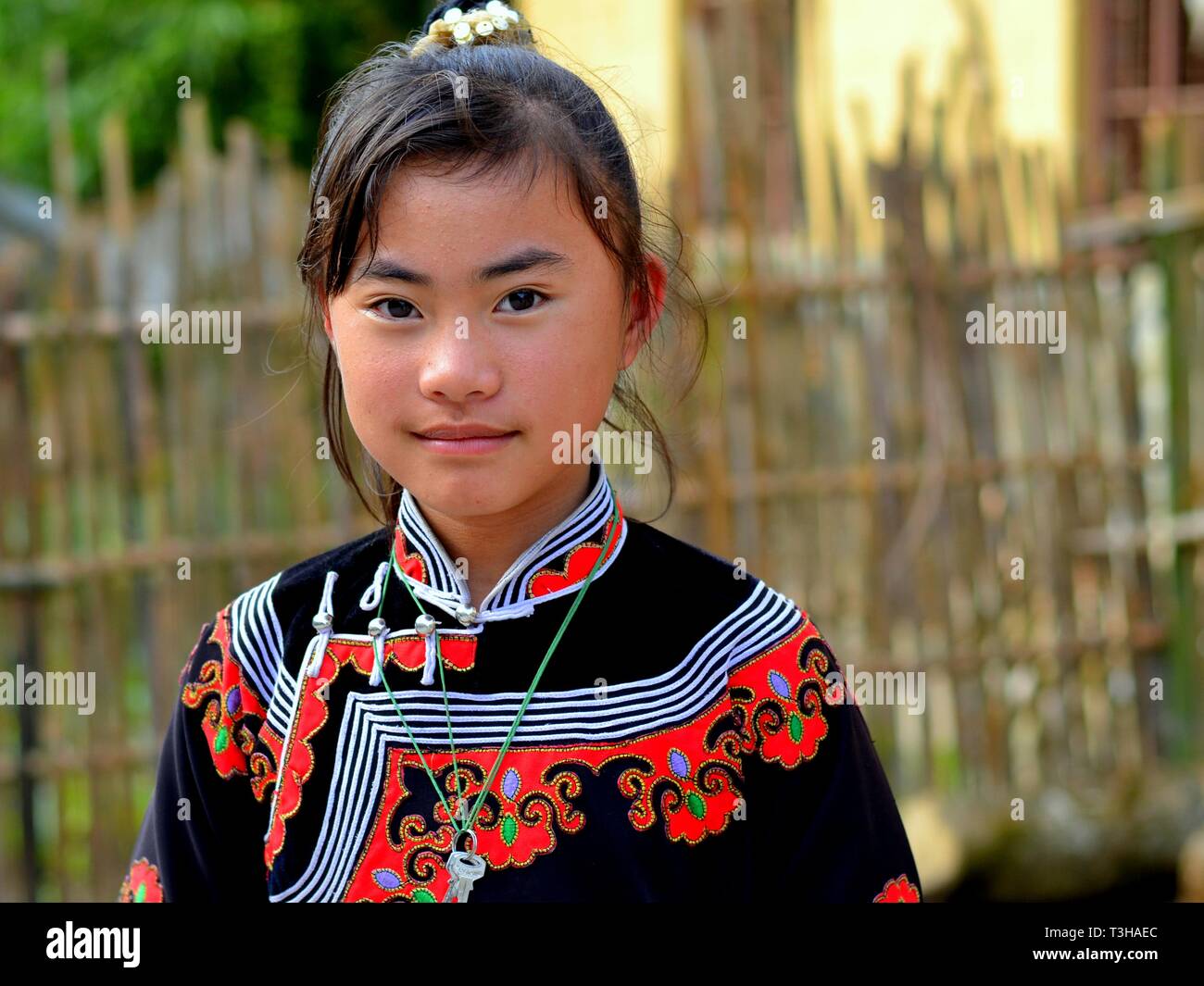 Pretty pre-teen Miao girl (Chinese ethnic minority) wears a red and black traditional ethnic dress and smiles for the camera. Stock Photo