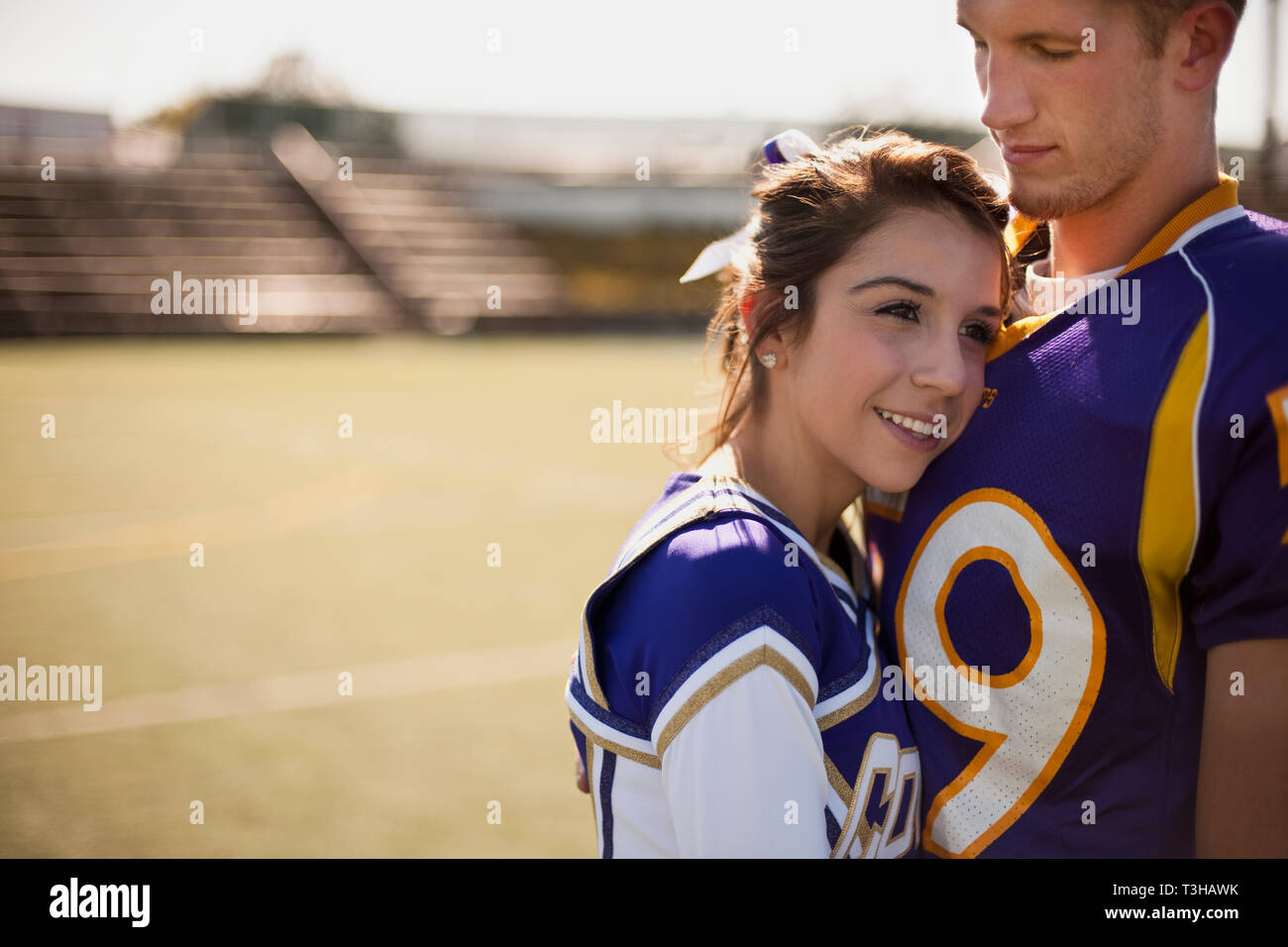 Cheerleader snuggled into football player's chest. Stock Photo