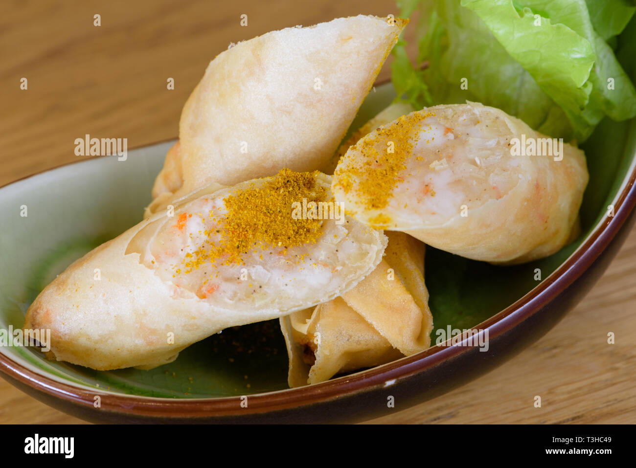 Harumaki, fried rolls in batter with shrimp pulp, flavoured with paprika, served with green salad on a boat-shaped plate Stock Photo