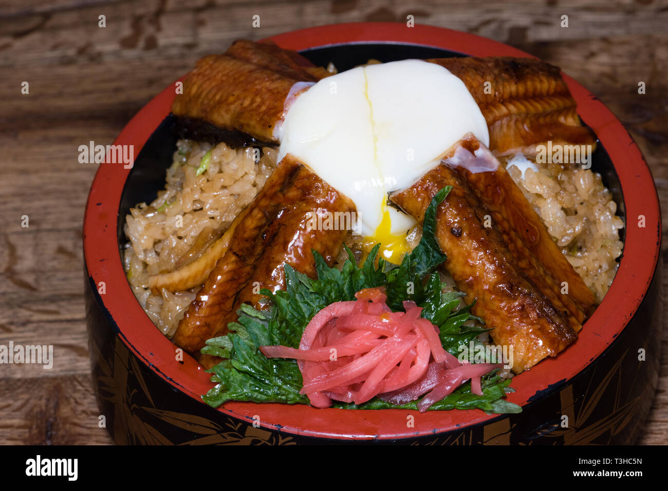Japanese fusion dish with spicy rice with tamari sauce, roasted eel, egg and red turnip, in a decorated bowl, dark wood table background Stock Photo