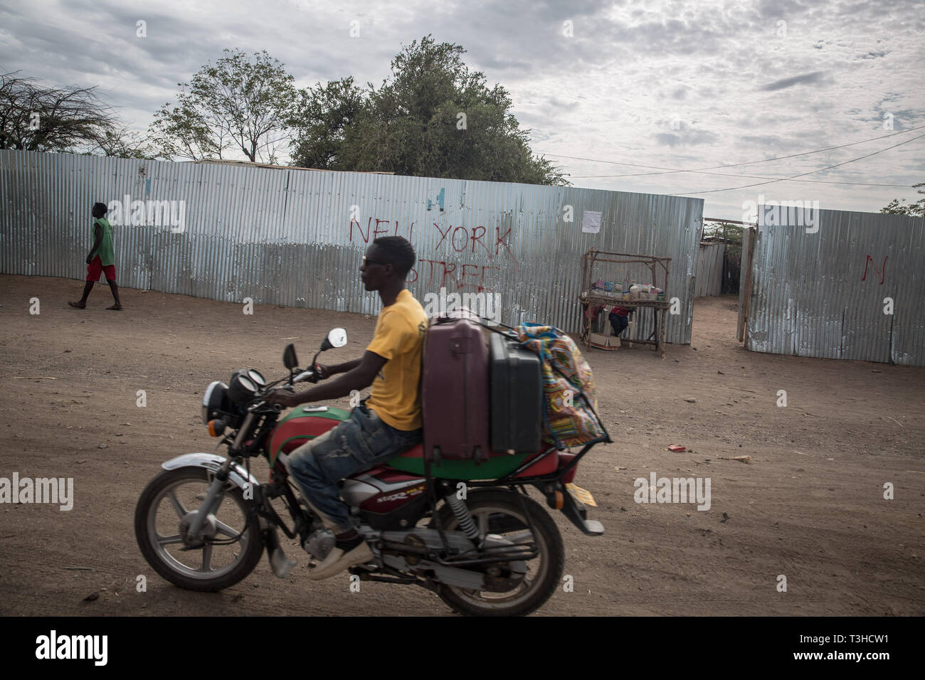 A boda boda rider seen riding along New York Street in Kakuma refugee camp, northwest Kenya. Kakuma is home to members of the local Turkana community and the nearby refugee camps shelter roughly 190,000 refugees from countries including Ethiopia, Burundi, Somalia, Tanzania and Uganda. Stock Photo