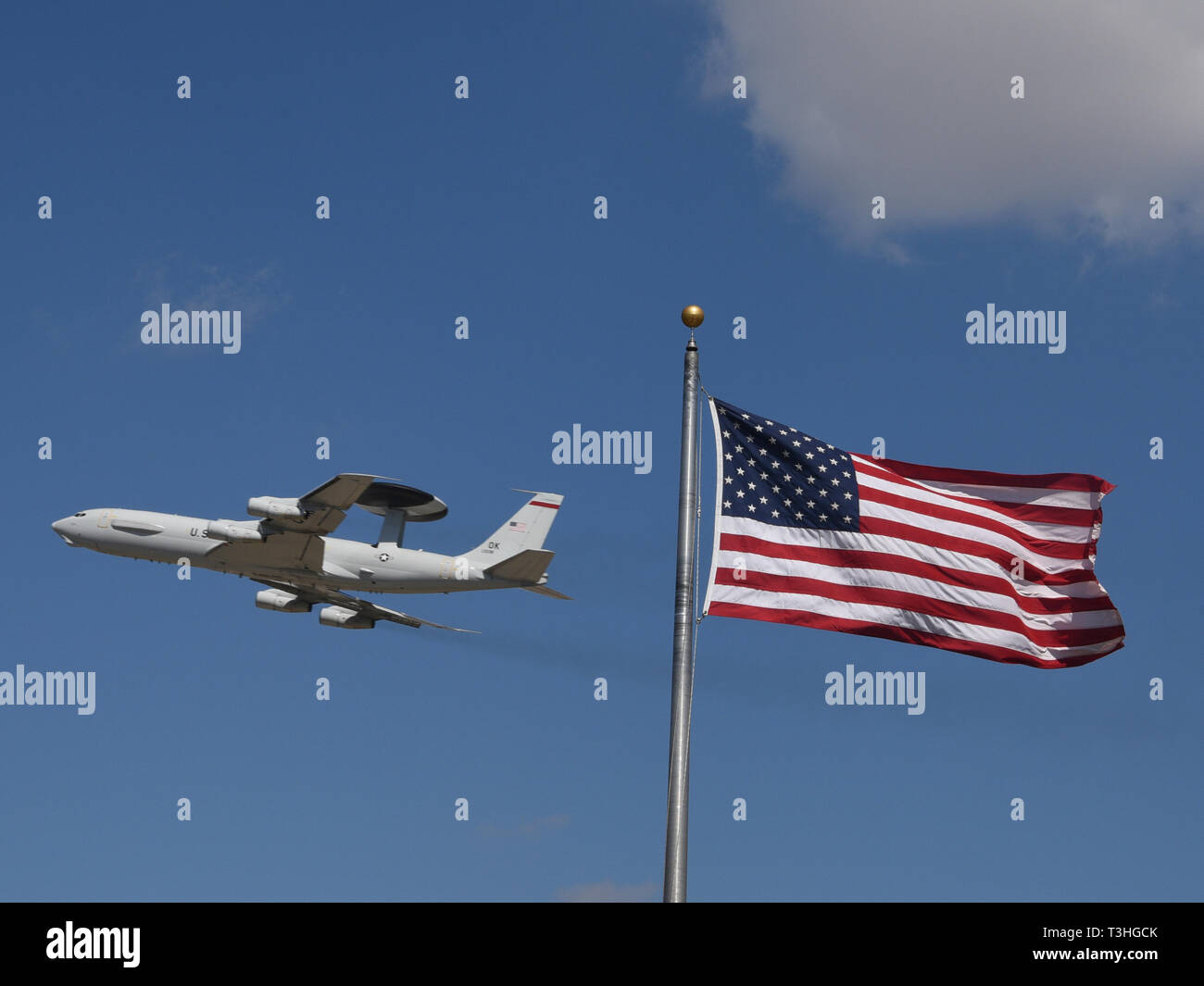 An E-3G Airborne Warning and Control System aircraft of the 552nd Air Control Wing, Air Combat Command, in-flight while conducting pilot proficiency training with the American flag flying in a strong wind in the foreground on March 20, 2019, Tinker Air Force Base, Oklahoma. The 552nd ACW is known as 'America's Wing' and their E-3 AWACS have called Tinker AFB home since March 23, 1977. (U.S. Air Force photo/Greg L. Davis) Stock Photo