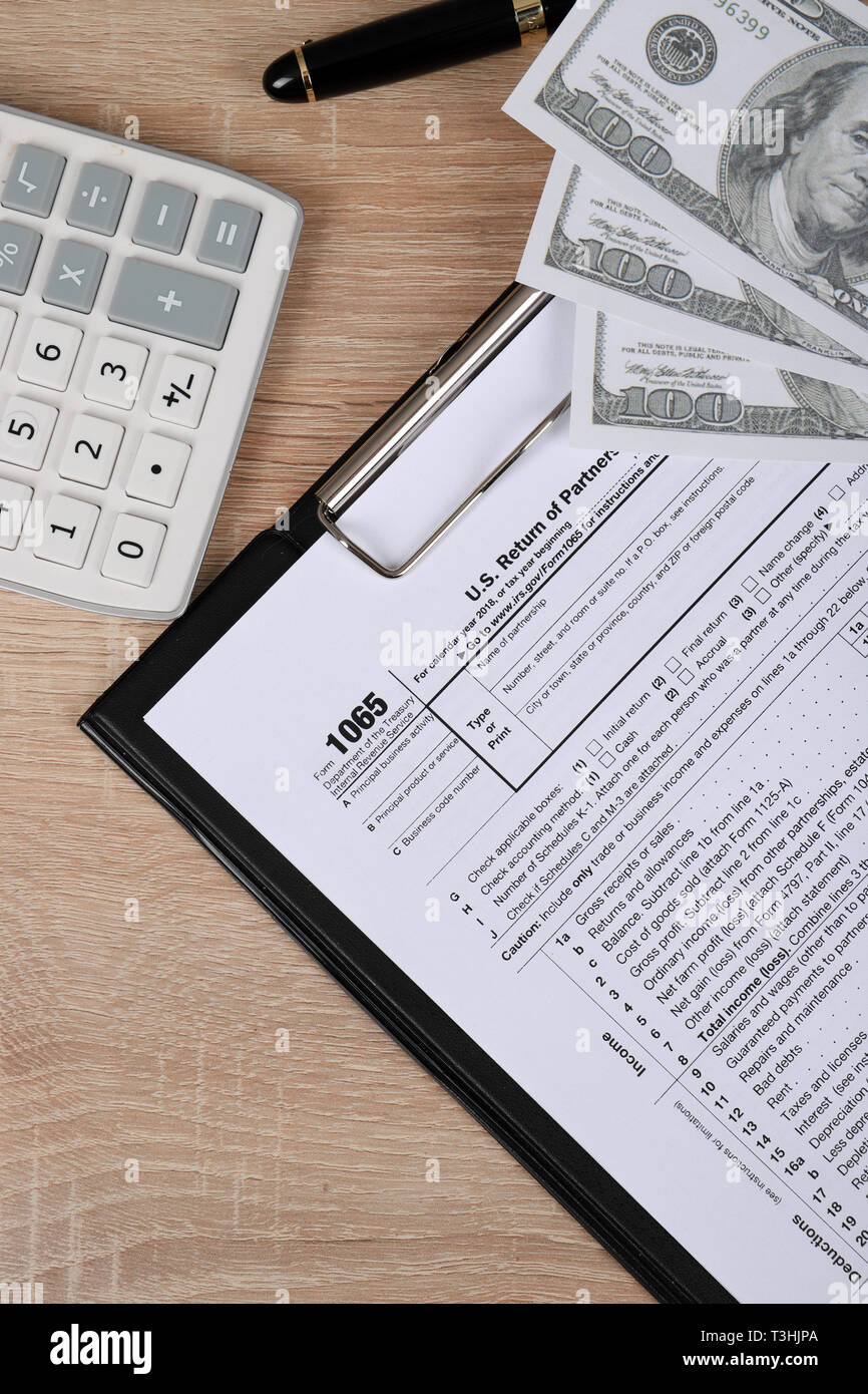 1065 tax form lies near hundred dollar bil and calculator  on a Table. US Return for parentship income Stock Photo