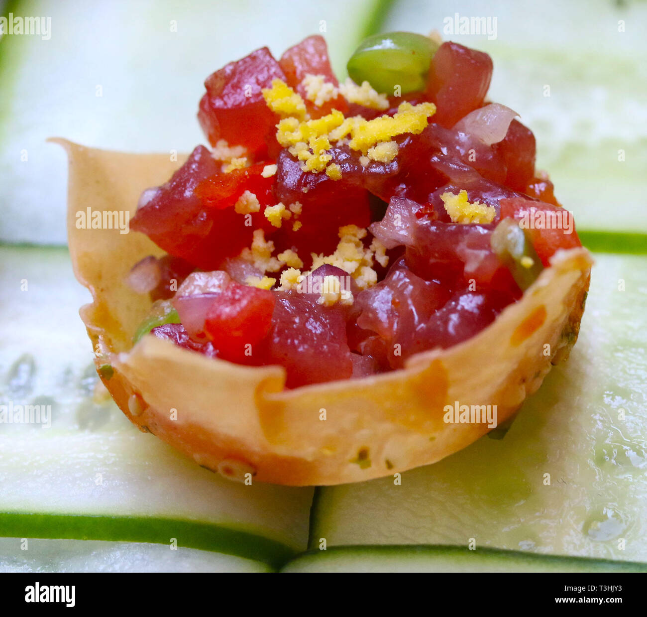 Raw tuna with vegetables and egg in a tortilla chip on cucumber slices
