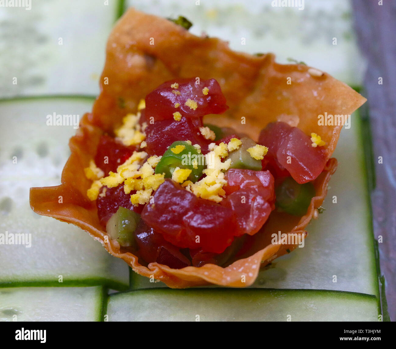 Raw tuna with vegetables and egg in a tortilla chip on cucumber slices