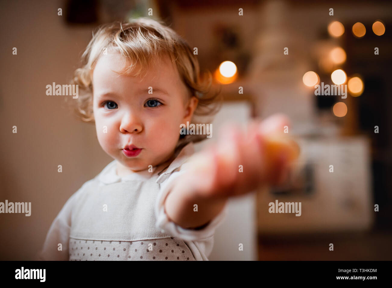 A small toddler girl sitting at the table, eating cakes at home. Stock Photo