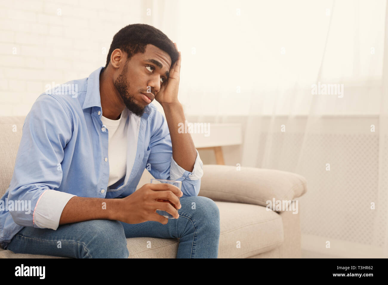 Young black man drinking alcohol at home feeling lonely Stock Photo
