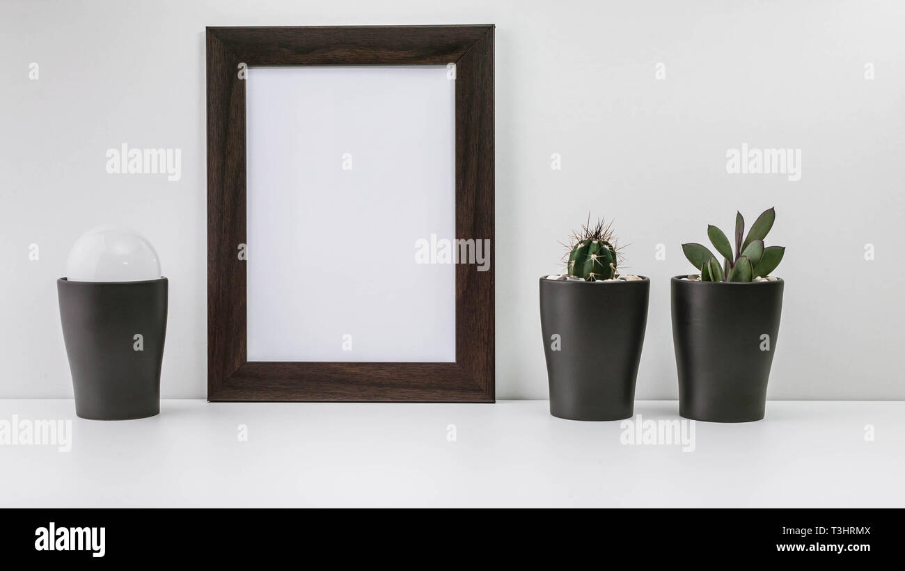 Empty dark photo frame, two succulents in dark pots and a white light bulb on a white background. Scandinavian style in the interior. Stock Photo
