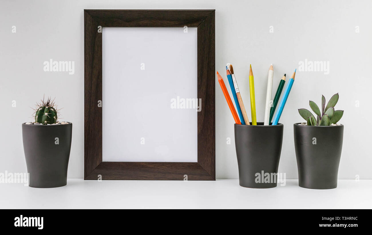 Empty dark photo frame, two succulents in dark pots and colored pencils on a white background. Scandinavian style in the interior. Stock Photo