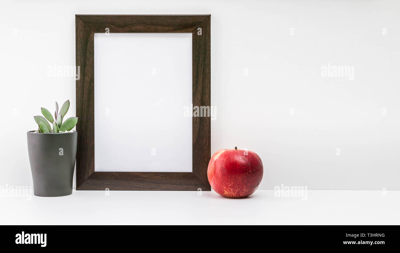 Empty dark photo frame, succulent in a dark pot and a red juicy apple on a white background. Scandinavian style in the interior. Stock Photo