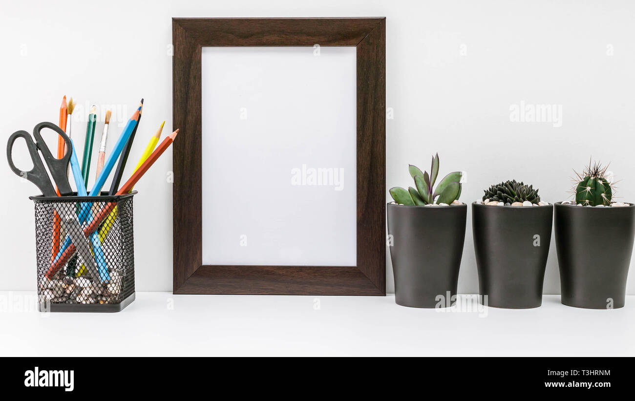 Empty dark photo frame, succulents in dark pots and colored pencils in the stand on a white background. MockUp. Scandinavian style in the interior. Stock Photo