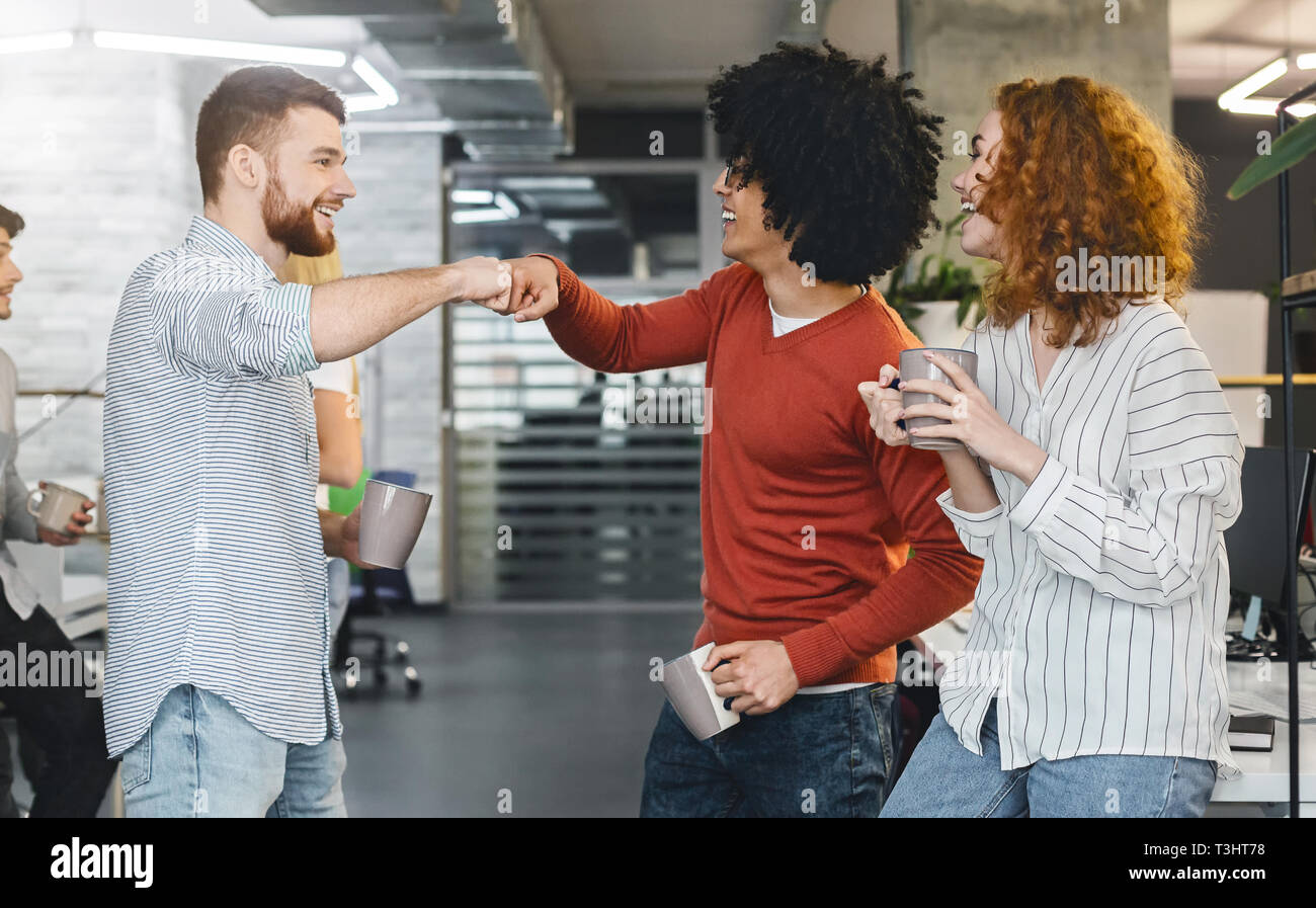 Happy male colleagues giving fist bump during coffee break Stock Photo