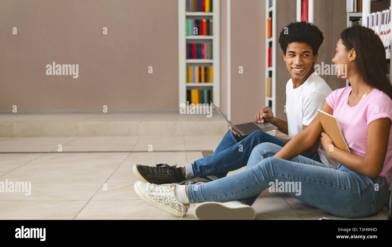 Smiling teenage couple sitting on floor in library Stock Photo