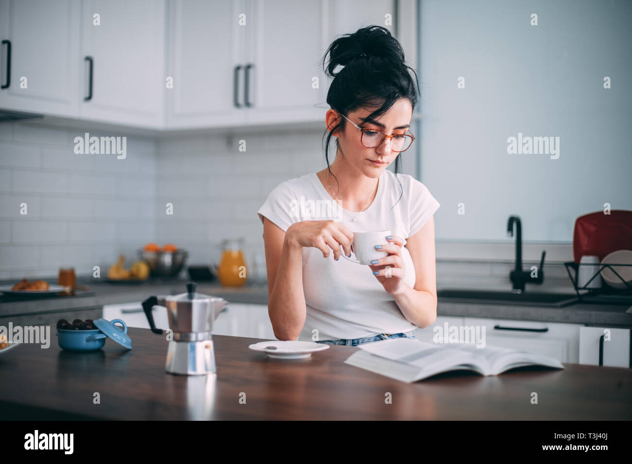 Beautiful young woman reading book in the kitchen Stock Photo