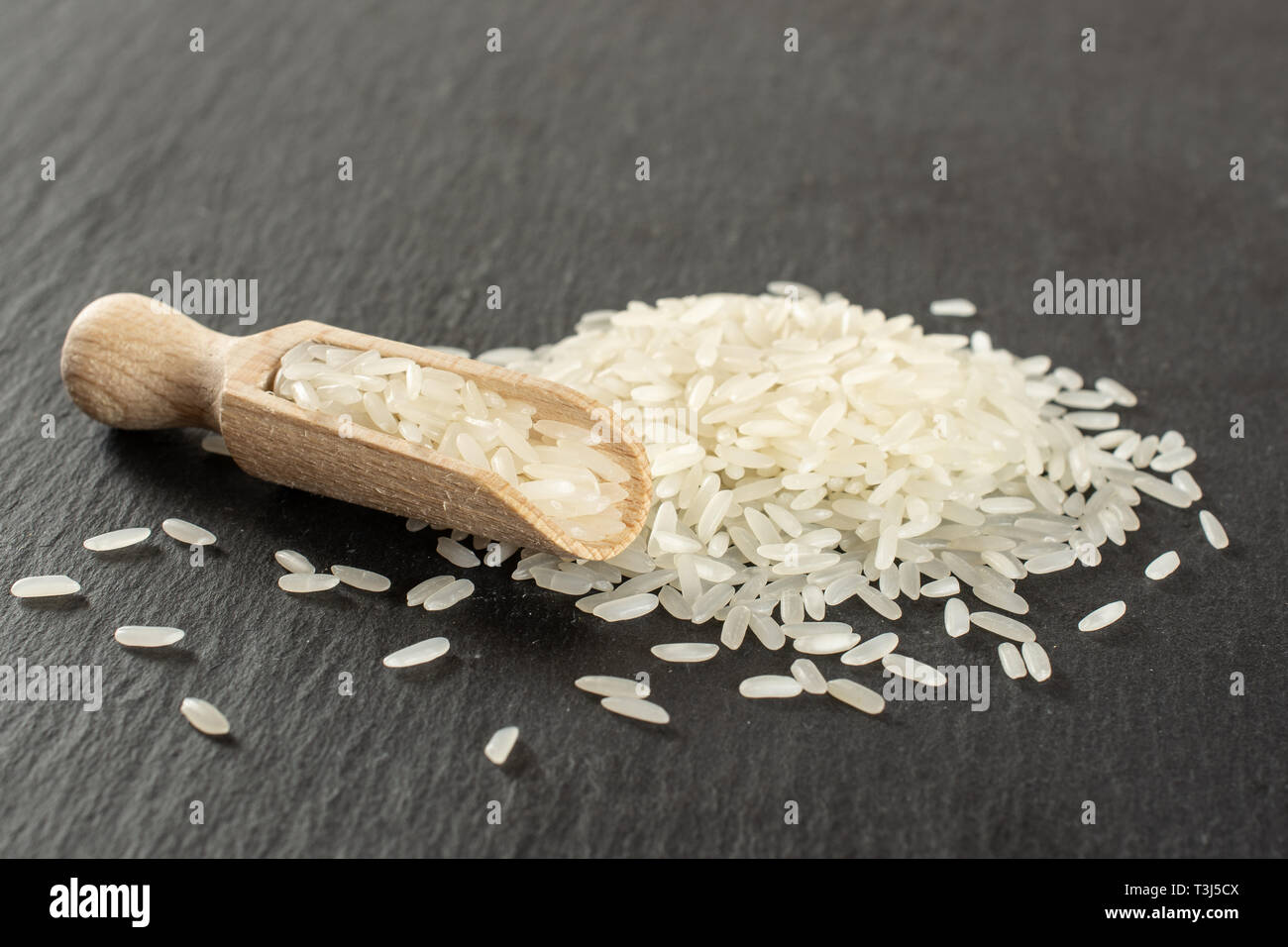 Lot of whole white jasmine rice grains with wooden scoop on grey stone